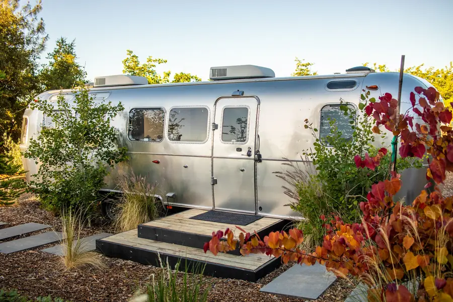 Airstream 2A with red autumn leaves and native plants by its steps