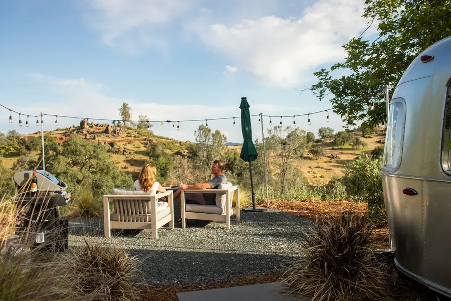 Outdoor chairs and string lights on the base-rock patio of Airstream 3A, looking out to the hills