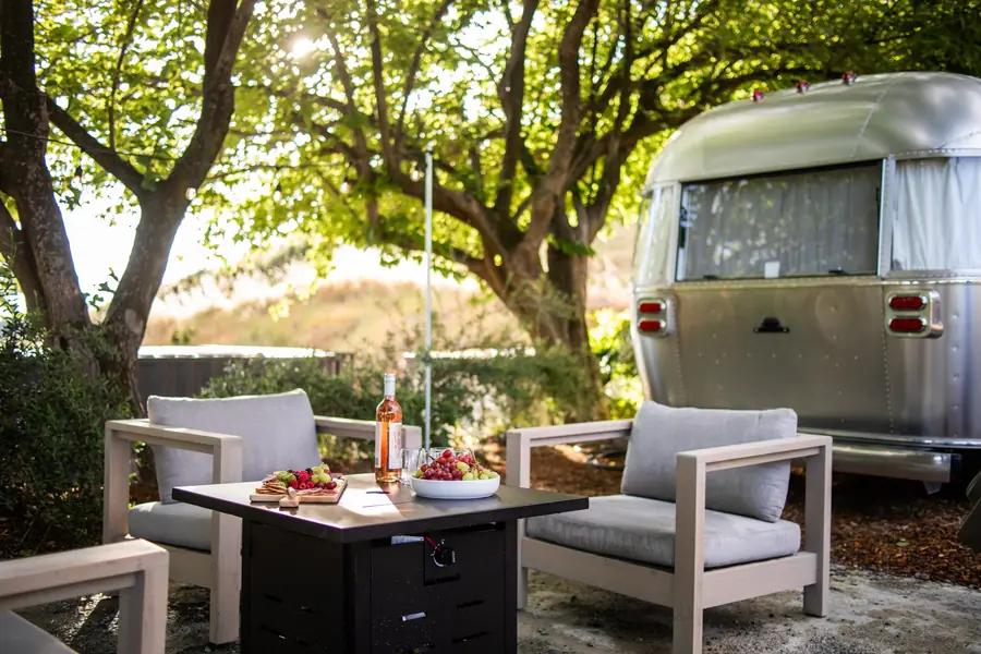 Lounge chairs around a propane fire table set with snacks beside Airstream 4A