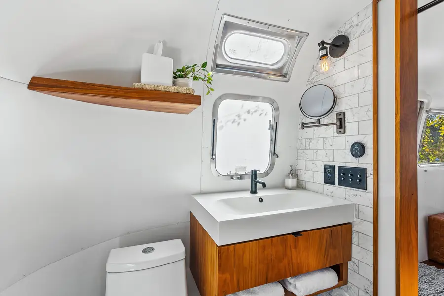 Airstream bathroom vanity with a white sink on a walnut cabinet, a round mirror and a small wooden shelf