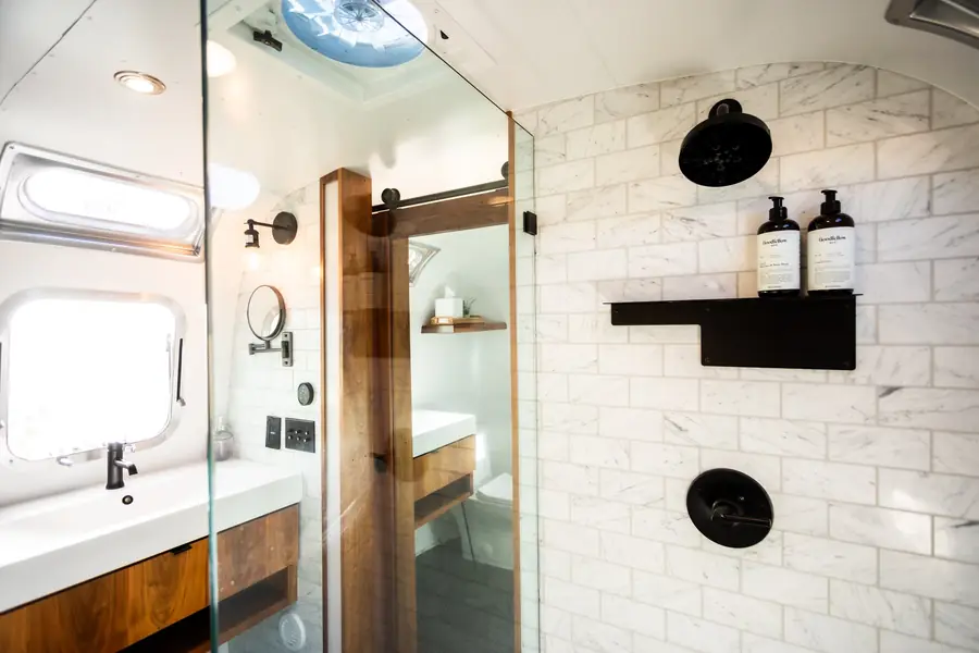 Airstream bathroom with white subway tile, a glass walk-in shower, black fixtures and a walnut vanity