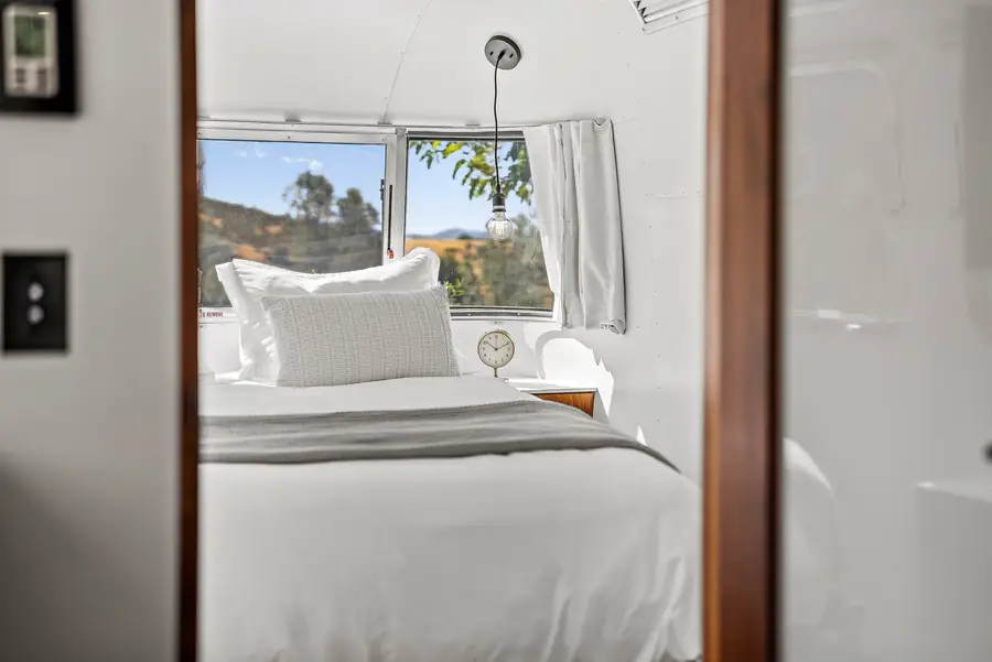 The queen bed seen through the bedroom doorway, with a window to the oak hills above the pillows