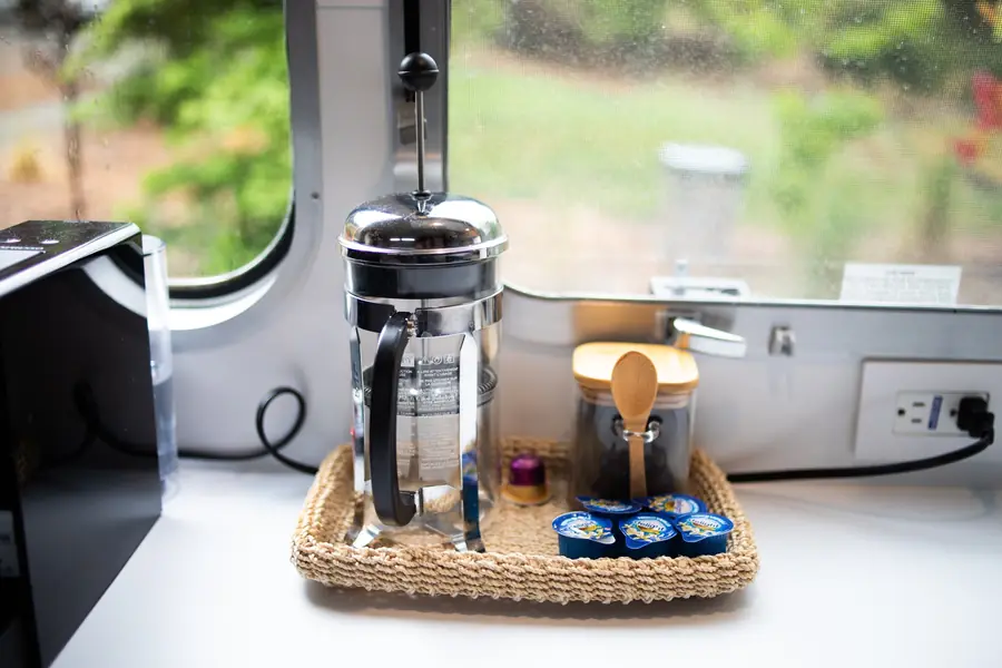 French press and a coffee tray with mugs on the kitchenette counter by a round window