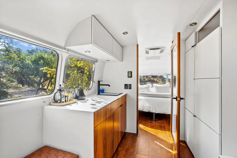 Wide view of the Airstream kitchenette with a walnut cabinet and white counter, looking back toward the bedroom
