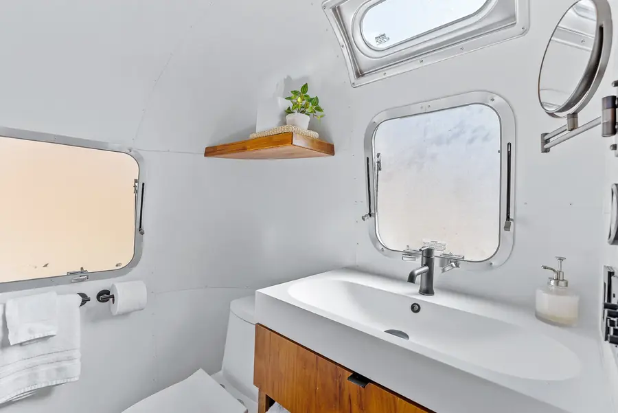 White sink on a walnut vanity under a porthole window, with a towel and a small plant on a shelf