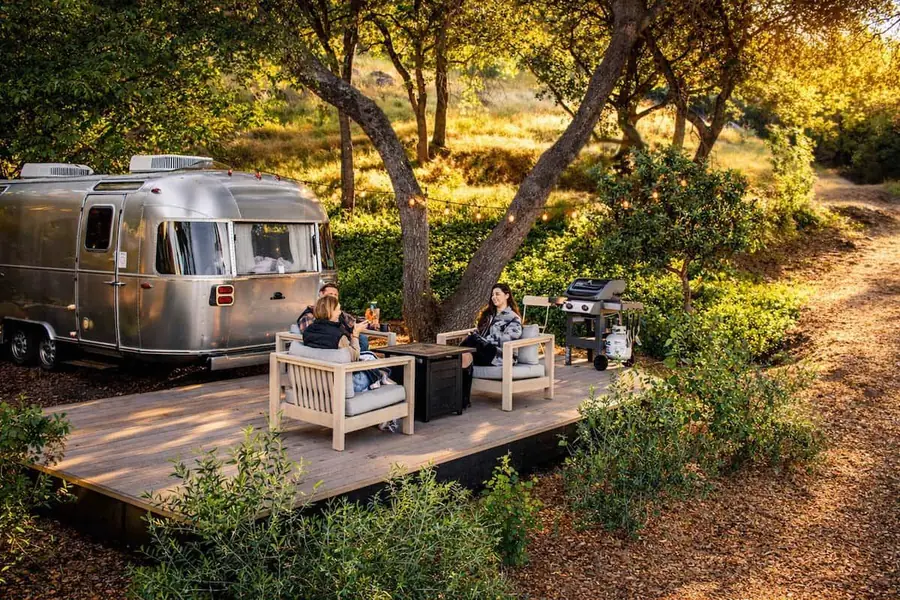 Airstream on a wooden deck under oak trees, with lounge chairs outside