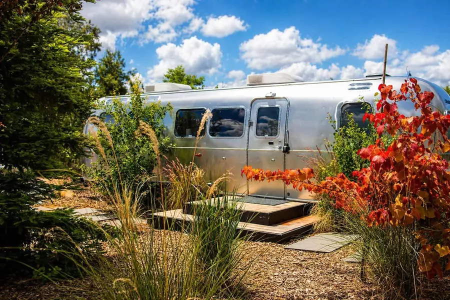 Airstream with native plants and red autumn leaves under a blue sky