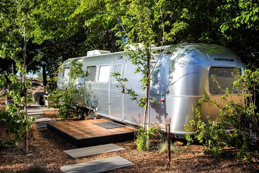 Airstream among green trees next to its private base-rock patio