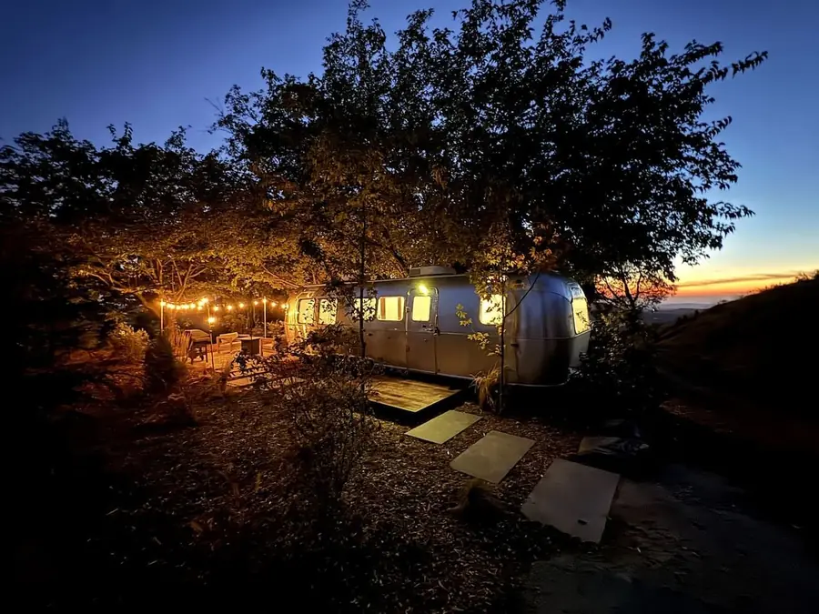 Airstreams glowing under oak trees at dusk beneath a deep blue sky