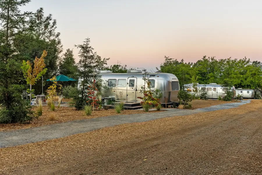 Five Airstreams in a row along a gravel path on the hillside at golden hour