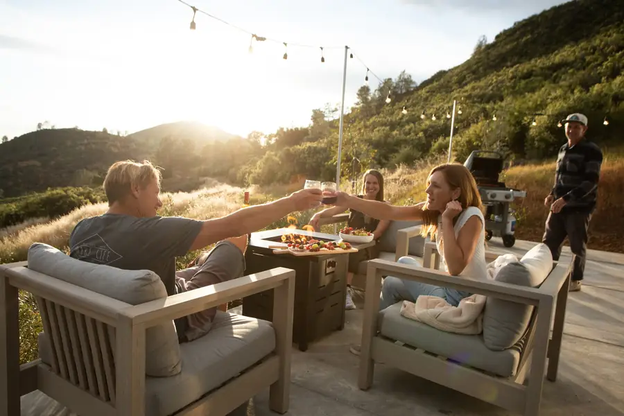Friends raising a toast around a propane fire table at sunset beside an Airstream