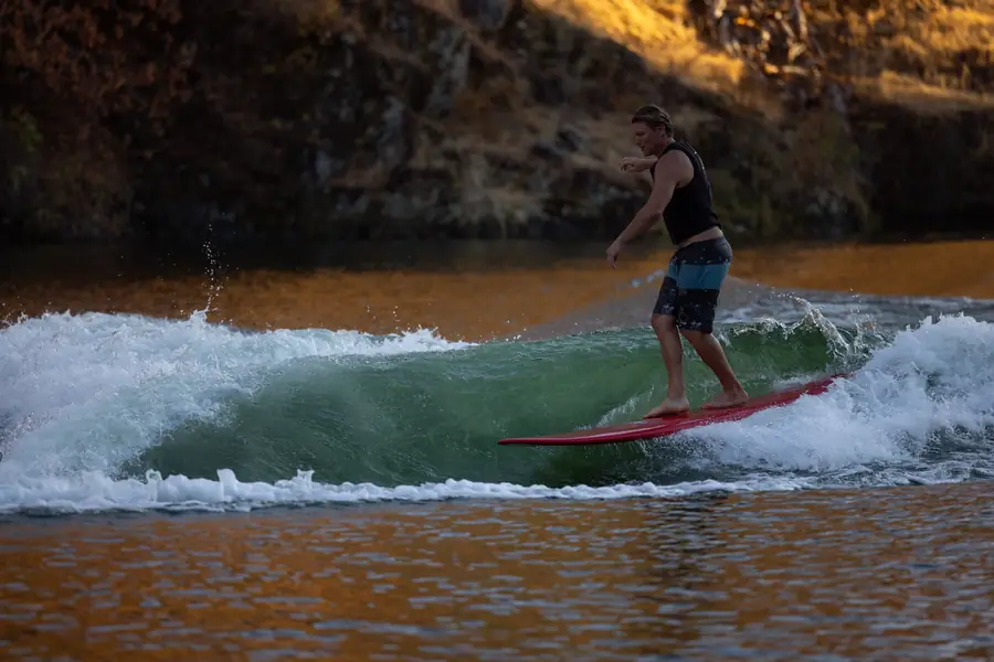 A wake surfer riding a green wave behind a boat on a foothill lake