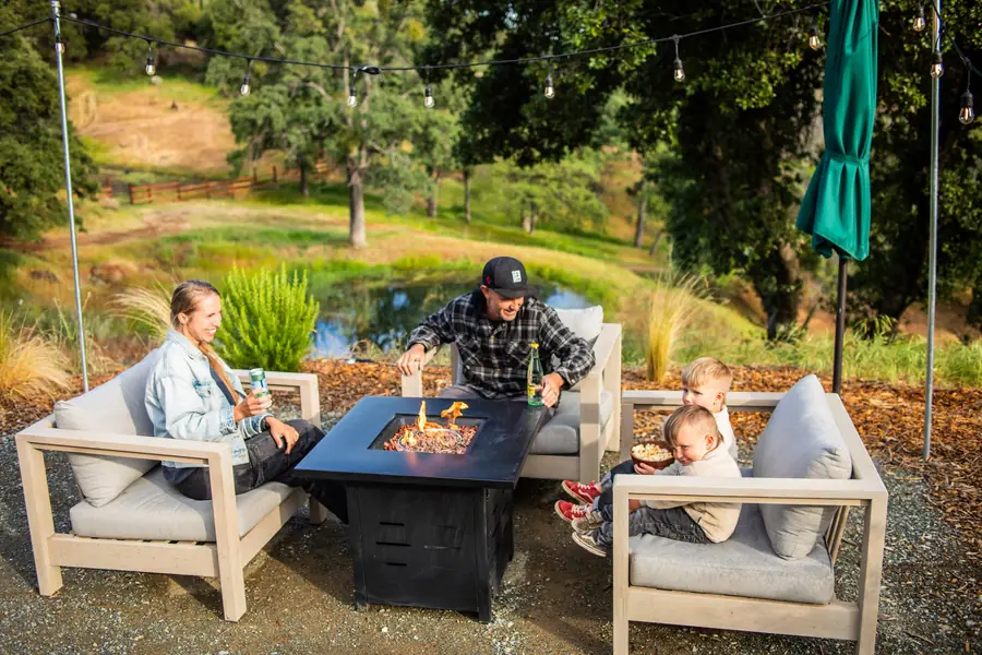 A family with young children gathered around a propane fire table outside their Airstream