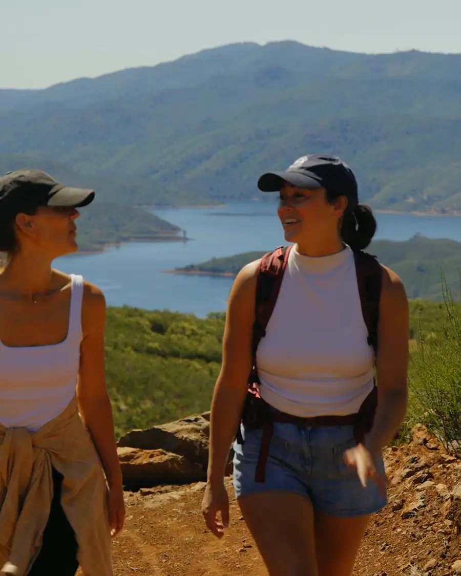 Two women laughing on a ridge trail with Lake McClure in the valley below
