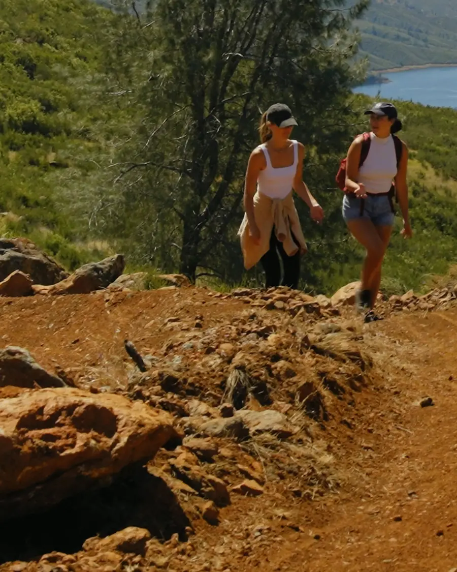 Two hikers on red rocks at a high point, with a glimpse of Lake McClure behind