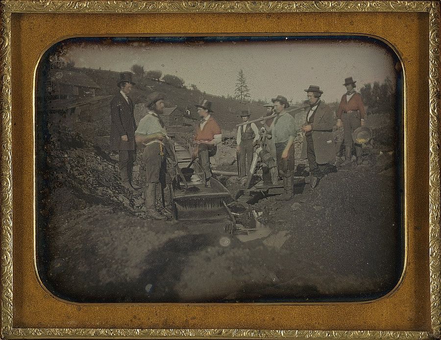 Daguerreotype in a brass frame of gold miners working a long wooden sluice, a long tom, beside a stream