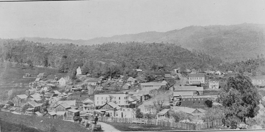 Old panorama of Coulterville's wooden buildings and Main Street below oak-covered hills