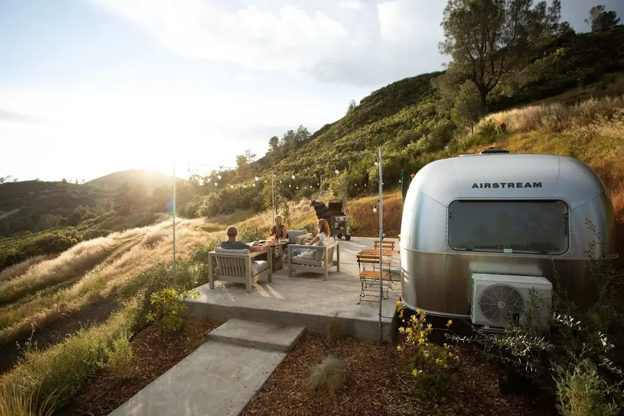 An Airstream and its outdoor space on a hillside above golden Sierra foothills at sunset