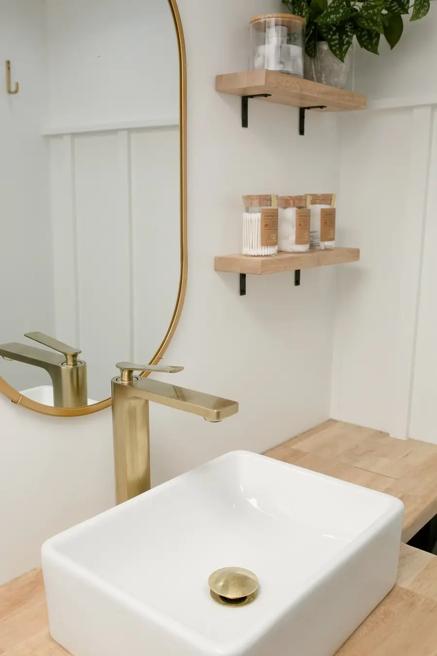 Bathroom in the Mariposa RV with a brass faucet, an oval mirror and wooden shelves
