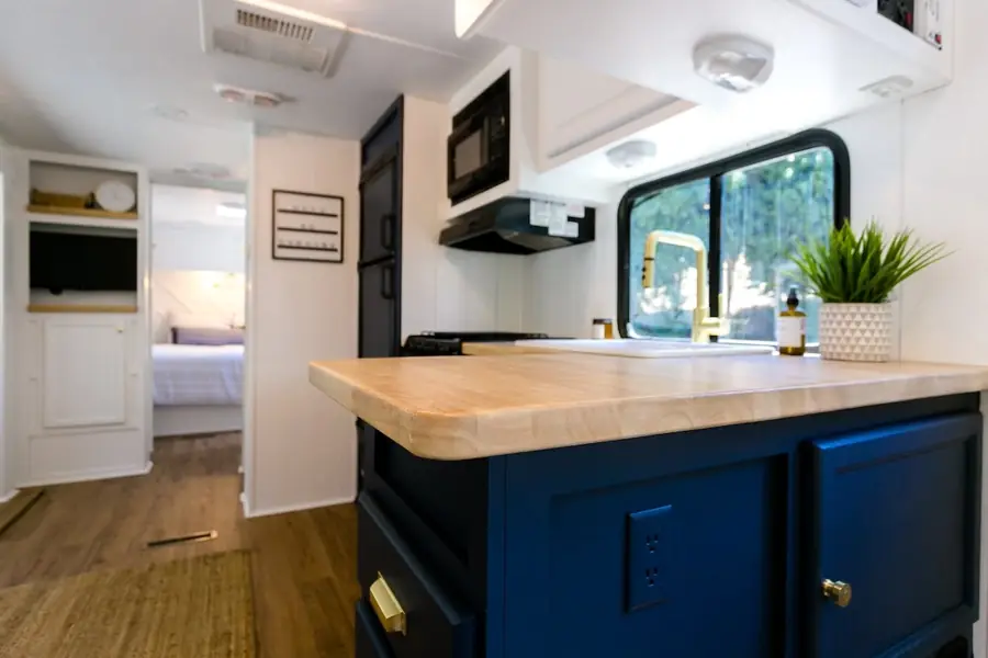 Inside the Mariposa RV: a navy kitchen island with a butcher-block top, with the bedroom beyond