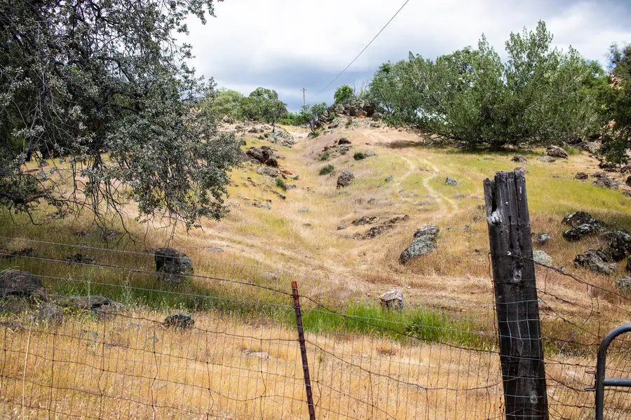 A private trail climbing a grassy hillside along a ranch fence